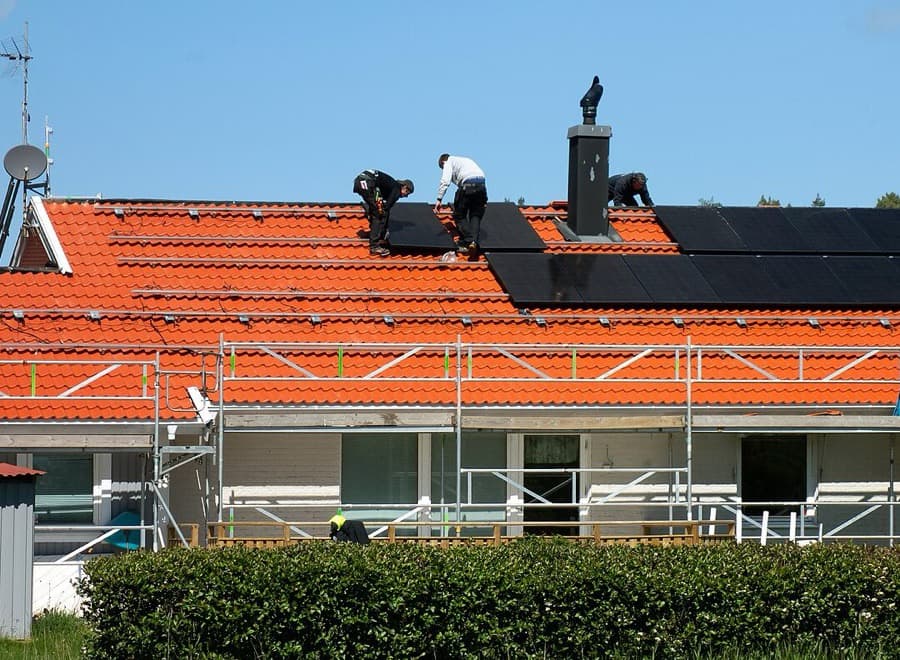 Drei Monteure installieren Solarmodule auf einem Ziegeldach